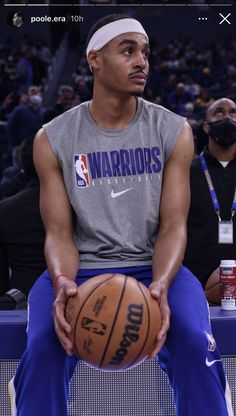 a man sitting on top of a basketball ball in front of an arena filled with people