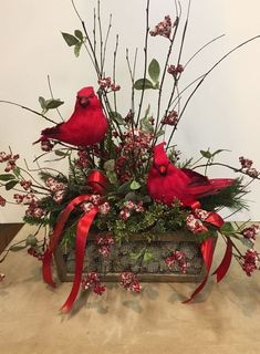 two red birds sitting on top of a wooden box filled with flowers and greenery