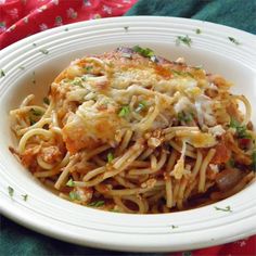 a white plate topped with pasta and meat covered in sauce on top of a green table cloth