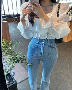 a woman taking a selfie in front of a mirror wearing high waist jeans and a white blouse