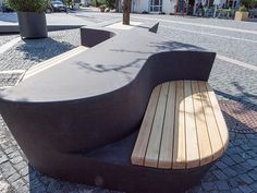 a wooden bench sitting on the side of a road next to a tree and buildings