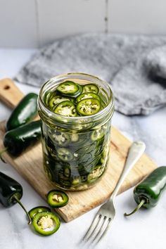 pickled jalapenos in a glass jar on a cutting board with spoons