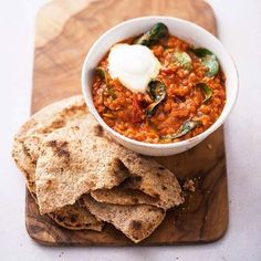 a wooden cutting board topped with a bowl of chili and tortilla chips