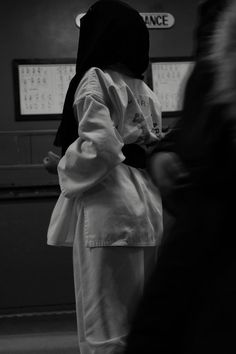 a person wearing a white coat and black hoodie standing in front of a wall