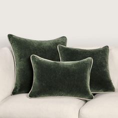 two green velvet pillows sitting on top of a white couch