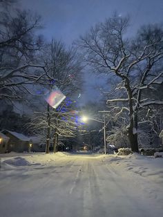 a snow covered street at night with the lights on and trees in the foreground