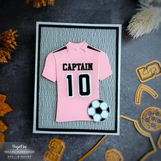 a card with a pink shirt and soccer ball on it, surrounded by other decorations