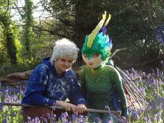 two people dressed as tinkerbells in a field of purple and green flowers