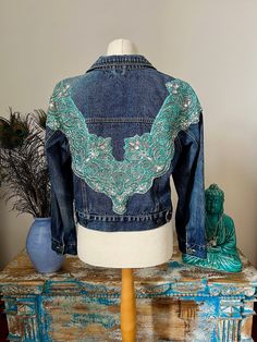 A lovely denim jacket that has been revamped using vintage Indian sari trim.  The jacket is a second hand noa noa jacket and in good condition. The decorative beaded panel on the back is a vintage Indian sari trim .  The jacket measures around the chest 100 cms . The length from mid shoulder to the hem 50 cms. Embellished Long Sleeve Denim Jacket For Festival, Bohemian Embellished Denim Jacket For Fall, Fitted Embroidered Denim Jacket For Festival, Fitted Bohemian Denim Jacket For Festivals, Bohemian Embellished Denim Jacket, Festival Embellished Fitted Denim Jacket, Blue Embellished Bohemian Outerwear, Embellished Denim Jacket, Upcycle Sewing