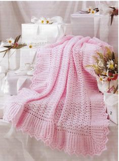 a pink crocheted blanket sitting on top of a bed next to white boxes