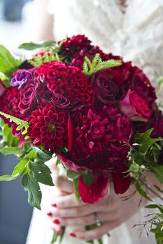 a woman holding a bouquet of red flowers in her hands and wearing a wedding dress