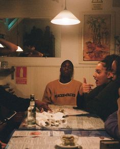 three people sitting at a table with food and drinks in front of them, one person pointing to the side