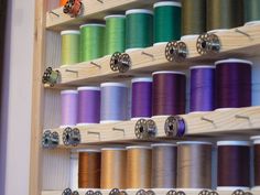 many spools of thread are on the wooden shelf next to each other in different colors