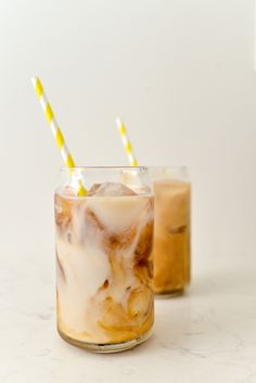 two glasses filled with iced coffee on top of a white counter next to each other