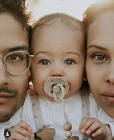 a man and woman holding a baby with a pacifier in front of their face