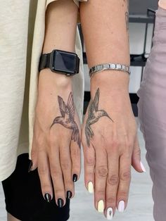 two women with matching tattoos on their hands holding each other's hand and looking at the camera