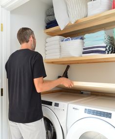 a man standing in front of a washer next to a dryer and shelves