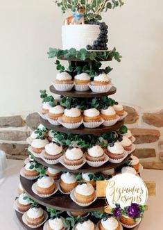 a tiered cake with cupcakes and greenery on top