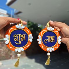 two people holding up small ornaments with the word india written on them in gold and blue