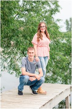 a young man and woman posing for a photo on a dock with trees in the background