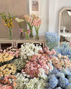 many different colored flowers in vases on a table next to a dresser and mirror