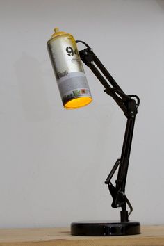 a black desk lamp with a yellow light on it's side and a white wall in the background