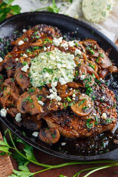 a pan filled with meat and mushrooms covered in parmesan cheese on top of a wooden table