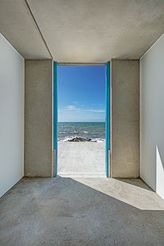 an open door leading to the beach with blue sky and water in the back ground