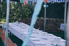 a long table set up with plates and glasses for an outdoor dinner or party event