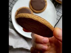 a person holding a cookie in front of some cookies on a white plate and cooling rack