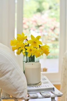 a glass vase with yellow flowers on a coffee table in front of a white chair