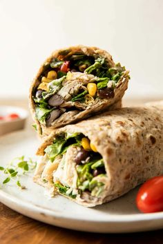 a burrito on a plate with tomatoes and lettuce next to the wrap