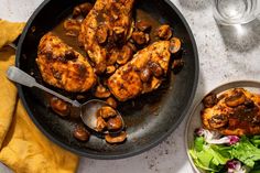 a pan filled with chicken and mushrooms on top of a table next to a bowl of salad