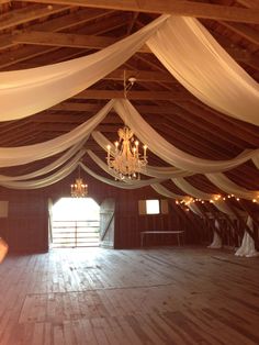 the inside of an old barn with chandelier and white drapes on the ceiling