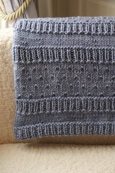 a gray knitted blanket sitting on top of a couch