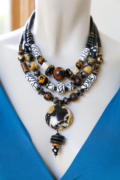 This unique safari statement necklace features mixed animal prints and stones in gold, chocolate, fawn, black, and white. I hand sculpted the beads from polymer clay, ensuring a one-of-a-kind necklace! The polymer clay beads are combined with glass and metal beads and strung onto cord. A brass lobster clasp finishes the necklace. All necklaces come gift wrapped, ready for gifting! Love animal prints? Check out my blooming animal print necklace here! https://www.etsy.com/listing/668349408/blooming-animal-print-statement-necklace?ref=related-2&frs=1 H A N D M A D E S T O R Y Every bead has been hand-shaped in clay, heat cured, and finished beautifully with a finishing glaze. The handmade beads are then carefully chosen, put together and strung onto cord. S I Z I N G This three layer necklace Diy Statement Necklace, Gold Statement Jewelry, Brown Beaded Necklace, Boho Styl, Diy Collier, Stone Statement Necklace, Cowgirl Jewelry, Blue Beaded Necklace, Bead Necklaces