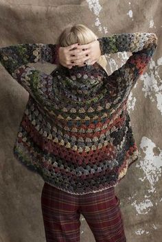 a woman is covering her face while standing in front of a wall with an overstuffed sweater on