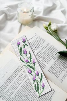 an open book with some flowers on top of it next to a candle and flower pot