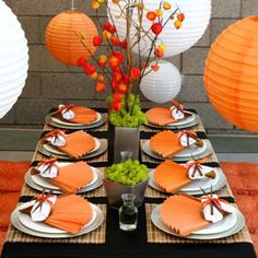 the table is set with orange and white plates, napkins, and paper lanterns