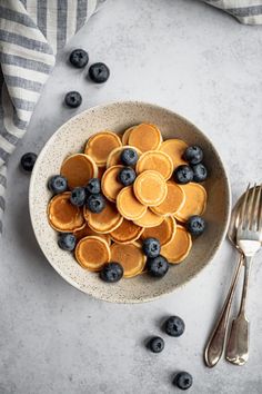 a bowl filled with blueberries and pancakes on top of a table next to silverware