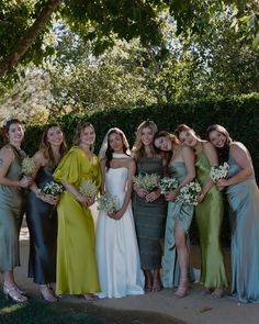 a group of women standing next to each other in formal dresses and holding bouquets