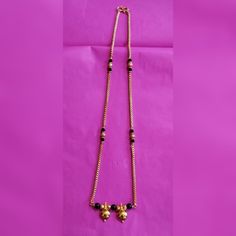 a long necklace with black beads and gold charms on a pink background, hanging from the side