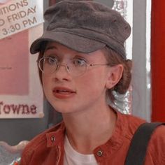 a young boy wearing glasses and a hat talking to someone in front of a sign