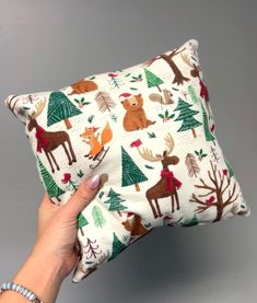 a person holding up a pillow with deer and trees on it