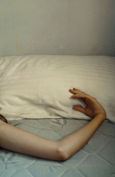 a woman laying on top of a bed under a pillow