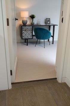 a blue chair sitting in the middle of a room next to a table with a lamp on it