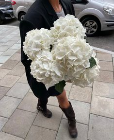 a woman is walking down the street holding a bouquet of white hydrangea flowers