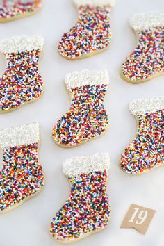 decorated cookies with sprinkles are arranged on a white tablecloth in the shape of christmas stockings