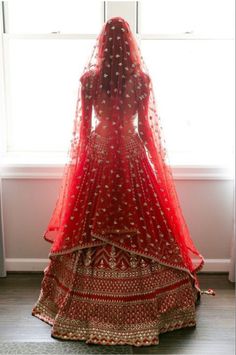 the back of a bride's red wedding dress standing in front of a window