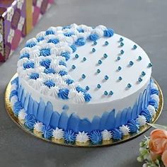 a blue and white frosted cake sitting on top of a table next to flowers